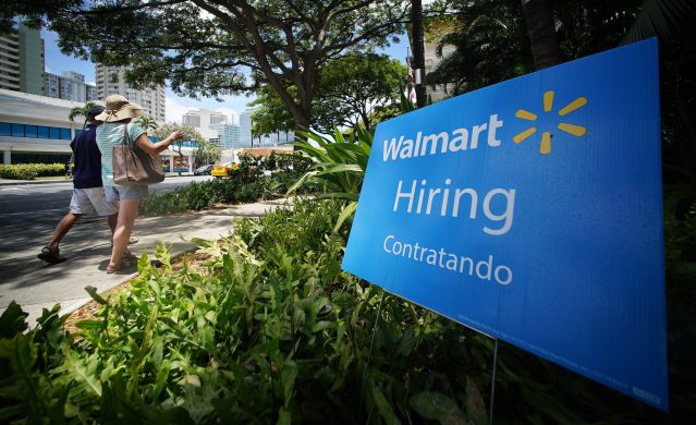 People stroll by on the sidewalk fronting a Walmart hiring sign along Keaaumoku Street.