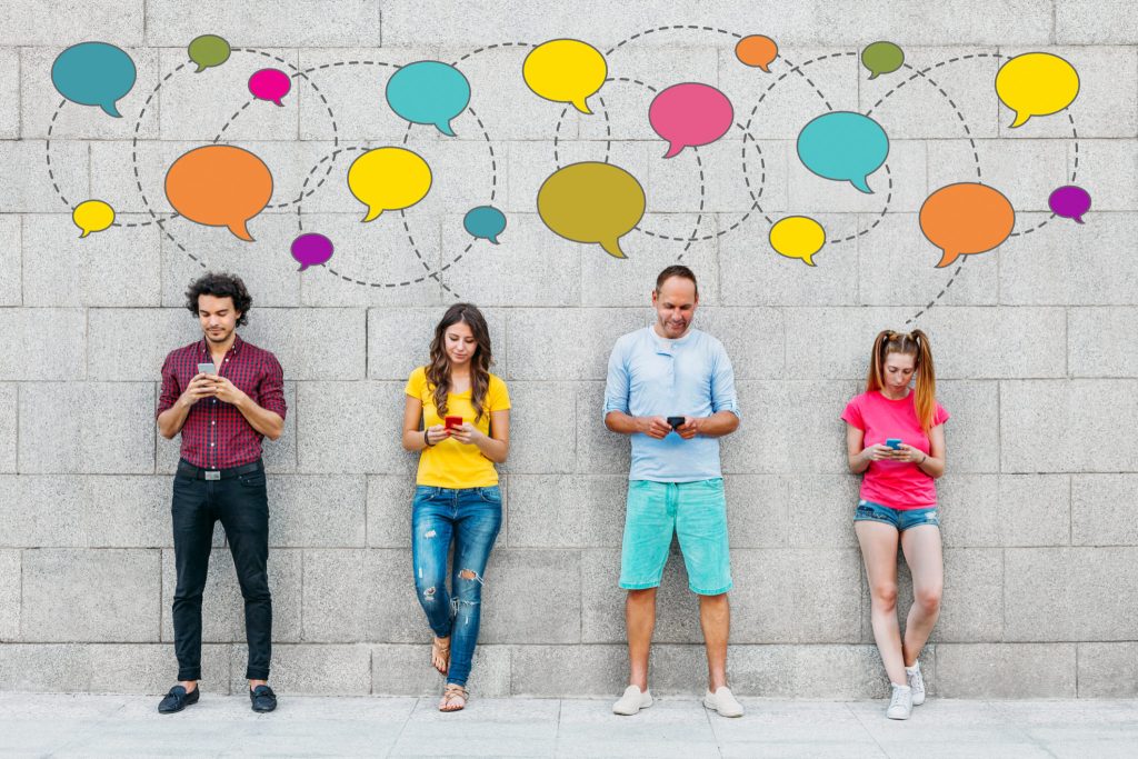 Social network concept. Young people texting with smart phones in front of big stone wall.