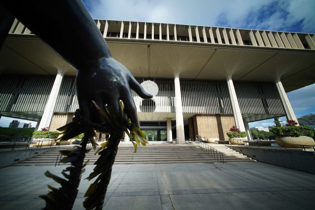 Lei bedecked bronze hand of Queen Liliuokalani on the makai side of the Hawaii State Capitol building.
