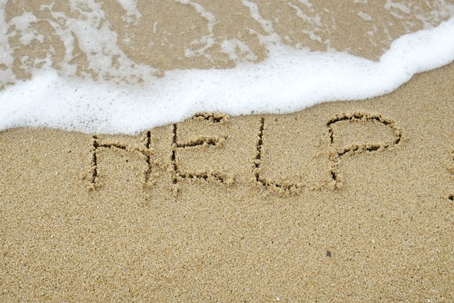 The word HELP written on sand being washed away by wave