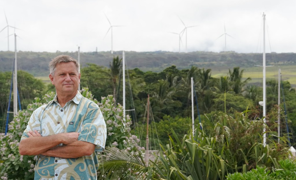 Senator Gil Riviere stands at Alii Park in Haleiwa with windmills above Waimea Bay on top of photograph.