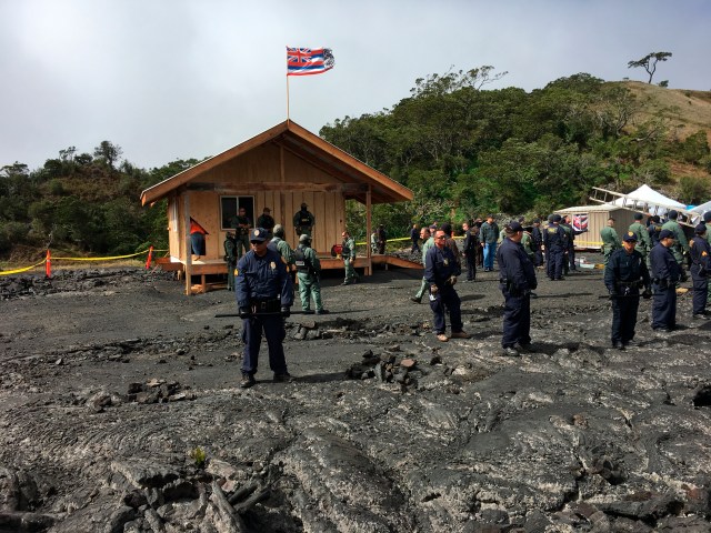 Crews and police gather at a lava field on Hawaii's Mauna Kea on the big island on Friday, Sept. 6, 2019 while a small wooden house is demolished. Opponents of a giant telescope built the unpermitted structure near their protest camp. (Dan Dennison/Department of Land and Natural Resources via AP)