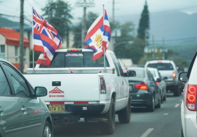 Truck drives down Kamehameha Highway in Kaneohe with Hawaiian flags attached to the bed.