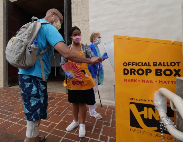 Kelly Dahling (center) a voter clerk, from the voter service center, opens the voting box so Honolulu resident Matthew Lindsey can cast his ballot at the Honolulu Hale, on Wednesday, August, 5, 2020. (Ronen Zilberman photo Civil Beat)