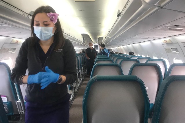 Masked Hawaiian Airlines stewardess cruises through the cabin which feature 3 people in the row due to COVID-19 pandemic. 2020