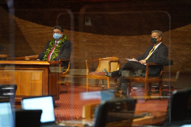Senate President Ron Kouchi and House Speaker Scott Saiki watch a large screen tv as Governor Ige gives the State of State address.