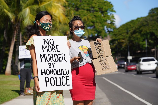 Cassie Chee and right, Cathy Lee hold signs in opposition to police shootings fronting Honolulu Hale with scores of others.