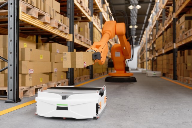 Automated Robot Putting Cardboard Box On AGV In Distribution Warehouse