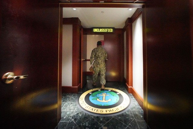 Navy personnel leads us into the Makalapa CINCPAC command center with sign about reading ‘Unclassified’.