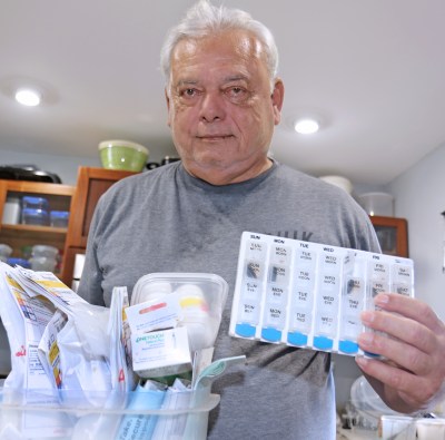 Roberto Garza of Hilo stands in his kitchen with his container of medicine. The U.S. Navy Veteran takes six prescriptions and insulin daily. Photo: Tim Wright