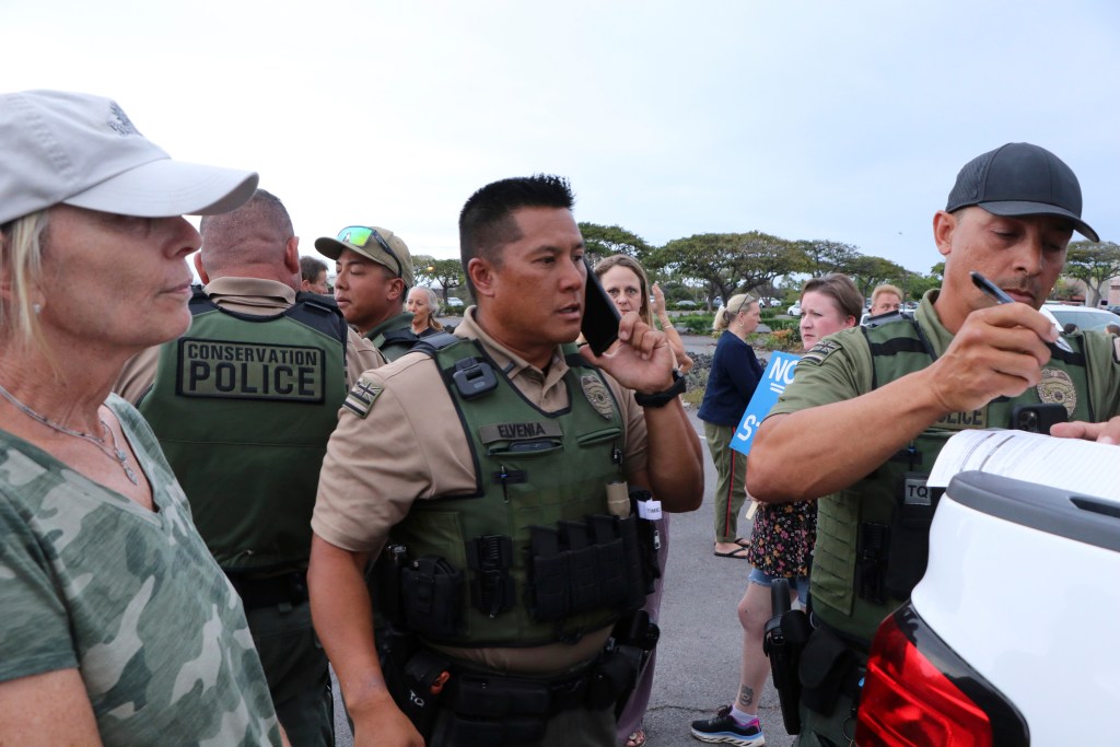 In this photo provided by the Hawaii Department of Land and Natural Resources, department law enforcement officers issue a citation to two women  at a Big Island shopping center parking lot, in Waikoloa, Hawaii, on Tuesday, April 18, 2023. State authorities cited the women for allegedly harming nene, an endangered species of geese native to Hawaii, by feeding feral cats in the lot.  (Dan Dennison/Hawaii Department of Land and Natural Resources via AP)