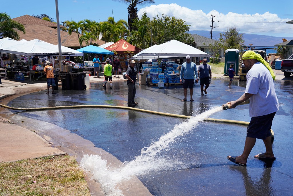 Wahikuli residents wash off ash and dust from the street Sunday, Aug. 13, 2023, in Wahikuli neighborhood, north of Lahaina town and south of Kaanapali. A large fire consumed areas of West Maui last week. Utilities have not been fully restored. (Kevin Fujii/Civil Beat/2023)