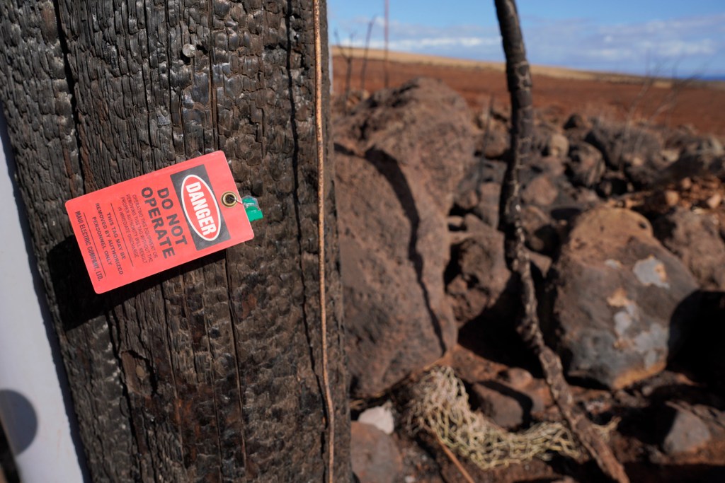 A MECO warning tag marks a utility pole in the area mauka of the Lahaina Bypass where a wildfire burned near a power station Sunday, Aug. 13, 2023, in Lahaina. A large fire consumed areas of West Maui last week. Utilities have not been fully restored. (Kevin Fujii/Civil Beat/2023)
