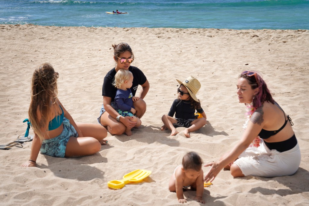 The Surfing Mom’s Victoria Moody, from left, Sachiko Stokes and Erica Diehl watch keiki Daniel Ritchie, Ekuale Taua’a and Santiago Martin as Esperanza Martin and her mom Melissa Martin paddle out during their weekly outing Tuesday, Aug. 15, 2023, at White Plains Beach in Ewa Beach. The moms take turn surfing while other moms watch the keiki. (Kevin Fujii/Civil Beat/2023)