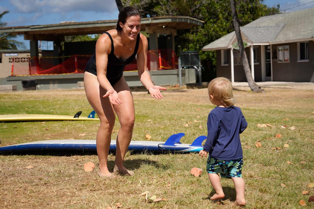 Surfing Mom Kelli Ritchie waits for a warm welcome from her son Daniel during the group’s weekly outing Tuesday, Aug. 15, 2023, at White Plains Beach in Ewa Beach. The moms take turn surfing while other moms watch the keiki. (Kevin Fujii/Civil Beat/2023)