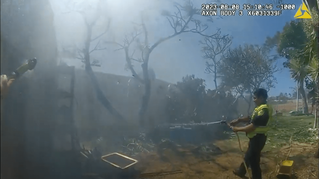 A Maui Police officer tries to put out a fire with a garden hose on Aug. 8, 2023. (Maui Police Body Camera/2023)