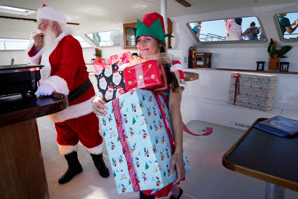 The crew of the Alii Nui Sunset Sail Santa Santa Claus grabs a snack while elf Robin Brown takes the wrapped presents to the deck of the Alii Nui. The sunset cruise during the holidays becomes the Santa Cruise. (Kevin Fujii/Civil Beat/2023)
