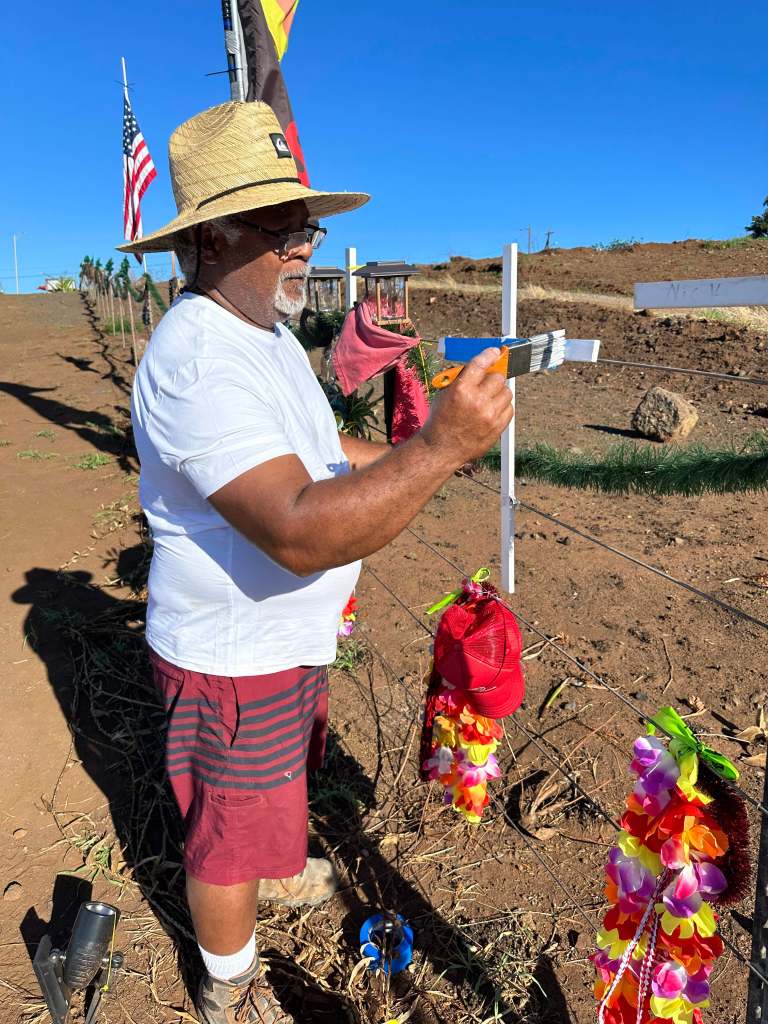 Soakai Taufa applied fresh paint to a cross on the roadside memorial to Lahaina wildfire victims on Saturday, 12/9/2023. Taufa, a carpenter, supplied the crosses for the grassroots effort. (Christie Wilson/Civil Beat/2023)