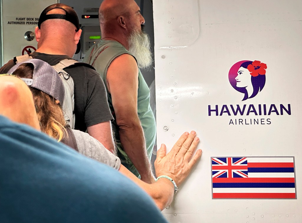 A passenger touches the exterior of a Hawaiian Airlines plane before take off Jan. 19, 2024, in Kahului. Alaska Airlines announced a $1.9 billion acquisition of Hawaiian Airlines late last year. (Kevin Fujii/Civil Beat/2024)
