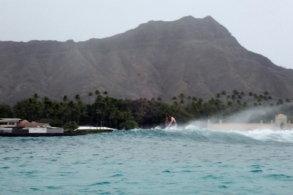 A surfer rides a wave at Queens break at Waikiki under Diamond Head Friday, April 5, 2024, in Honolulu. A wind advisory created unfriendly high winds for surfing. But some surf breaks in town had stiff, off-shore wind. (Kevin Fujii/Civil Beat/2024)