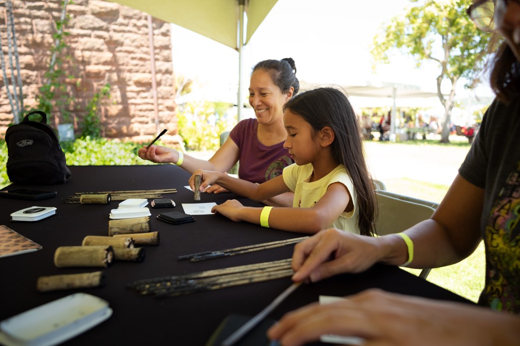 Kathy Kawelu and her daughter Kiliwehi Coyle of Hilo stamp patterns at FestPac at the Bishop Museum Sunday, June 8, 2024, in Honolulu. (Kevin Fujii/Civil Beat/2024)
