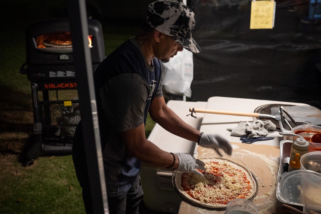 Tizza Pizza’s Tipa Cabus builds a cheese pizza at Ewa by Gentry Community Association’s Movie in the Park Friday, July 26, 2024, in Ewa Beach. Tabatha and Tipa Cabus operate the family run business. Numerous families attended to watch the animated film, “Migration,” and share dinner with family, friends and neighbors. (Kevin Fujii/Civil Beat/2024)