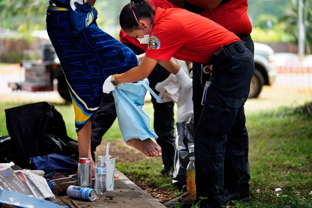 Honolulu C.O.R.E. EMT Bethany Nakano helps a homeless patient put on pants outside of Adventist Health Castle hospital Monday, Aug. 19, 2024, in Kaulua. (Kevin Fujii/Civil Beat/2024)