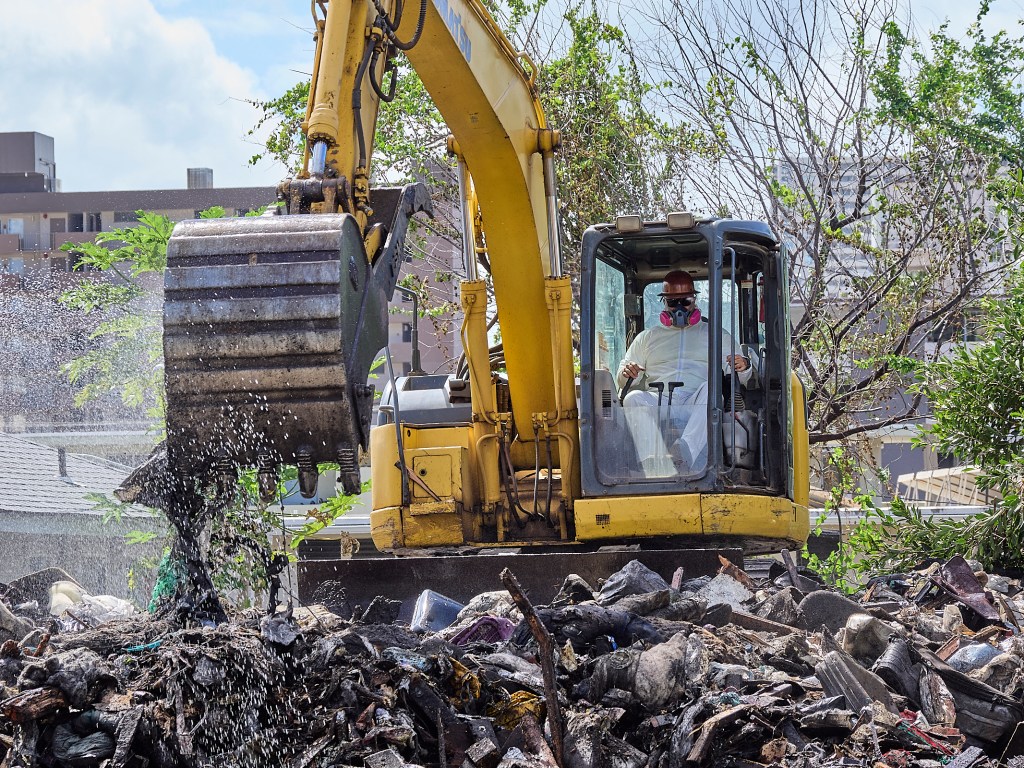 The two houses located at 1421 Pensacola Street had developed into hoarder houses where all kinds of trash, from cardboard boxes to old furniture items were strewn around the property. On at least one occasion the area succumbed to fire endangering nearby properties. On August 22nd 2024 the City and County brought in an excavator to demolish the piles of rubbish that had accumalated leaving a putrid smell in its wake. (David Croxford/Civil Beat/2024