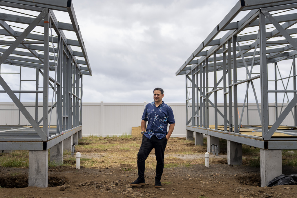 Kuhio Lewis, CEO of the Council for Native Hawaiian Advancement, stands for a portrait between two under-construction modular housing units at the Ke Ao Maluhia housing development, Monday, July 8, 2024, in Kahului, Hawaii. (AP Photo/Lindsey Wasson)