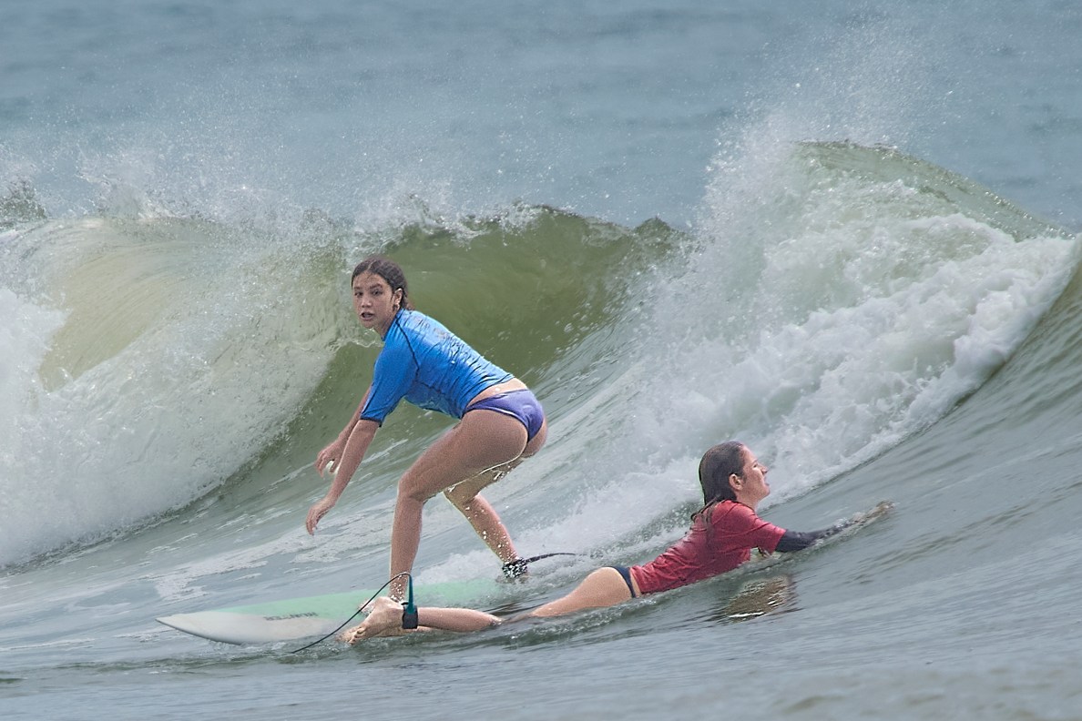 High School surfing started its season at Ala Moana Bowls on Saturday October 26th, 2024 with 17 schools competing in the day long event. In the girls short board event Kara Watson (Blue) takes off on a wave as Solbee Ahina (Red) paddles out.(David Croxford/Civil Beat/2024)