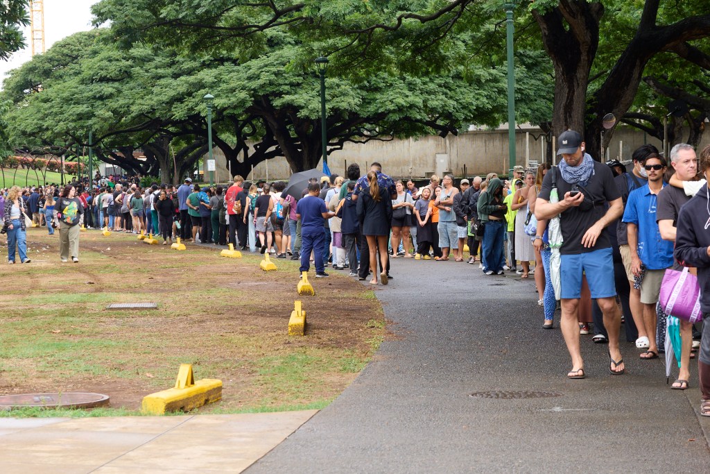 Voters at Honolulu Hale on King Street in Honolulu were met with Poll workers as they drove through the election only lane that had been set aside and coned to allow drivers to either hand off their ballots to Poll workers or drop them into several Ballot boxes placed and manned along King Street.  The lines snaked around the rear of Honolulu Hale, out to the walkway in the rear and then went all the way to Ala Wai and back providing wait times in excess of 2 hours (David Croxford/Civil Beat/2024)