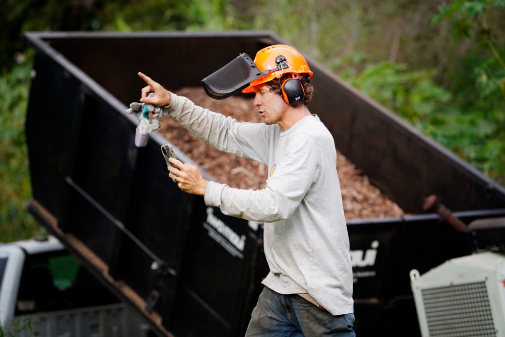 Mālama Kula Executive Director Kyle Ellison (orange helmet) uses his phone to update Maui’s Upcountry recovery process Friday, Nov. 8, 2024, in Kula. This mostly residential, non-tourist area was hit with a fire the same day as Lahaina on Aug. 8, 2023. (Kevin Fujii/Civil Beat/2024)
