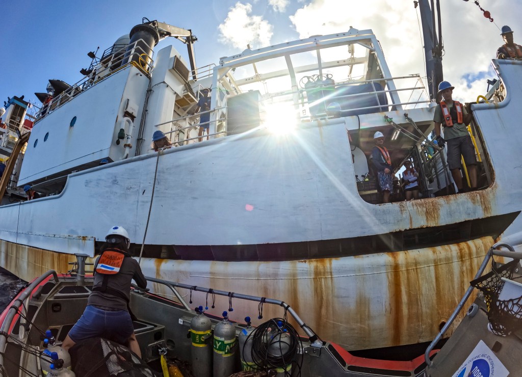 Scientist Atsuko Fukunaga, foreground at left, ties up the small rigid hull inflatable boat to the Oscar Elton Sette, NOAA's research vessel. (Nathan Eagle/Civil Beat/2024)