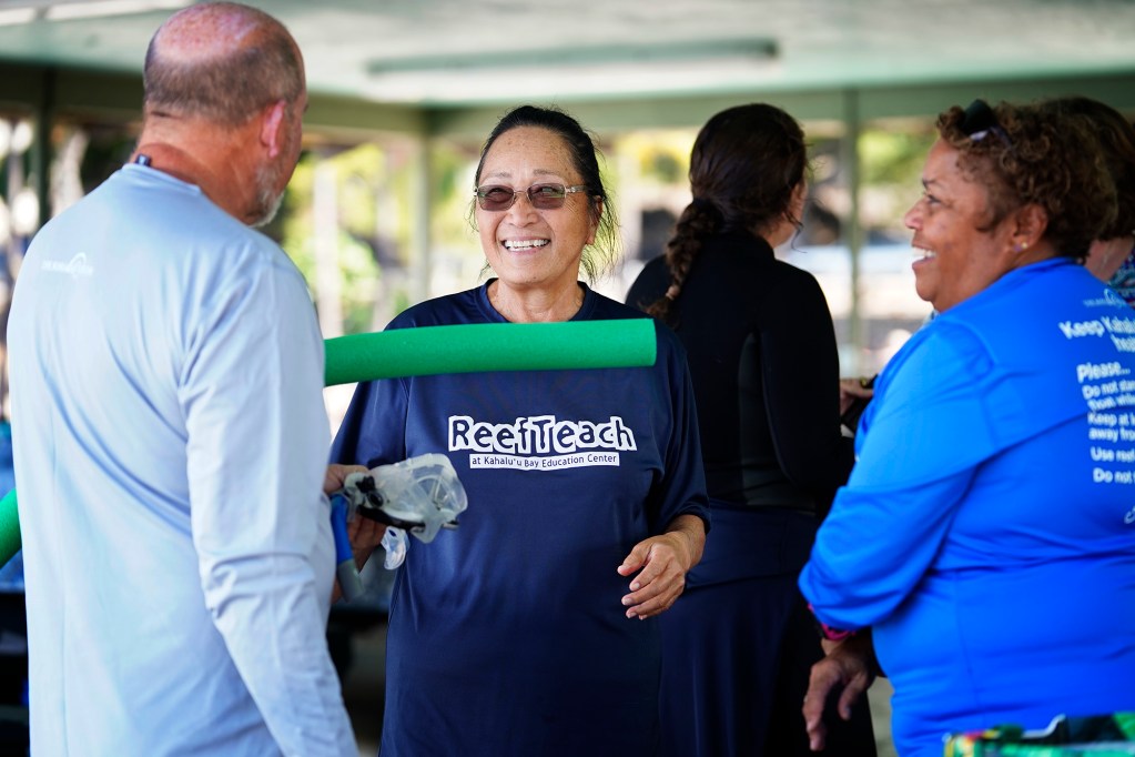 Paul Morrison of Sonoma, Calif., talks story with ReefTeach at Kahalu’u Bay Education Center’s Cindi Punihaole and Sheryl Robinson at Kahalu’u Beach Park Wednesday, Dec. 11, 2024, in Kailua-Kona. ReefTeach educates visitors to about protecting the sensitive corals and greater bay infrastructure. (Kevin Fujii/Civil Beat/2024)