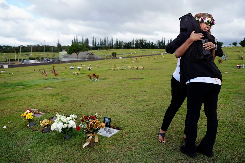 Lucita Ani-Nihoa, left, hugs Mae Nani Knight at Theresa Cachuela’s grave Sunday, Dec. 15, 2024, at the Mililani Memorial Park and Mortuary in Mililani. The mother and best friend of Theresa invited Civil Beat to visit her gravesite almost one year after she was killed by her estranged husband Jason Cachuela despite a temporary restraining order. (Kevin Fujii/Civil Beat/2024)
