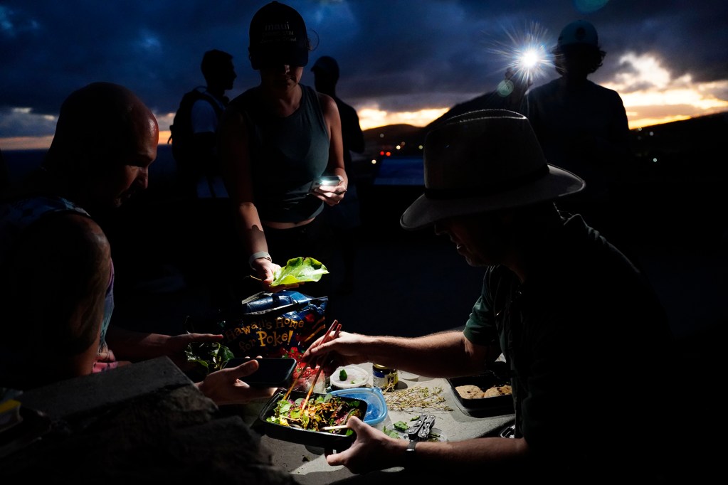 The sun sets as Dr. Nat Bletter, right, serves up a salad with greens found during his Urban Foraging in Honolulu's Jungles class Sunday, Dec. 15, 2024, in Honolulu. A hallmark of Dr. Bletter’s class is to only harvests invasive or overly abundant endemic plants. (Kevin Fujii/Civil Beat/2024)