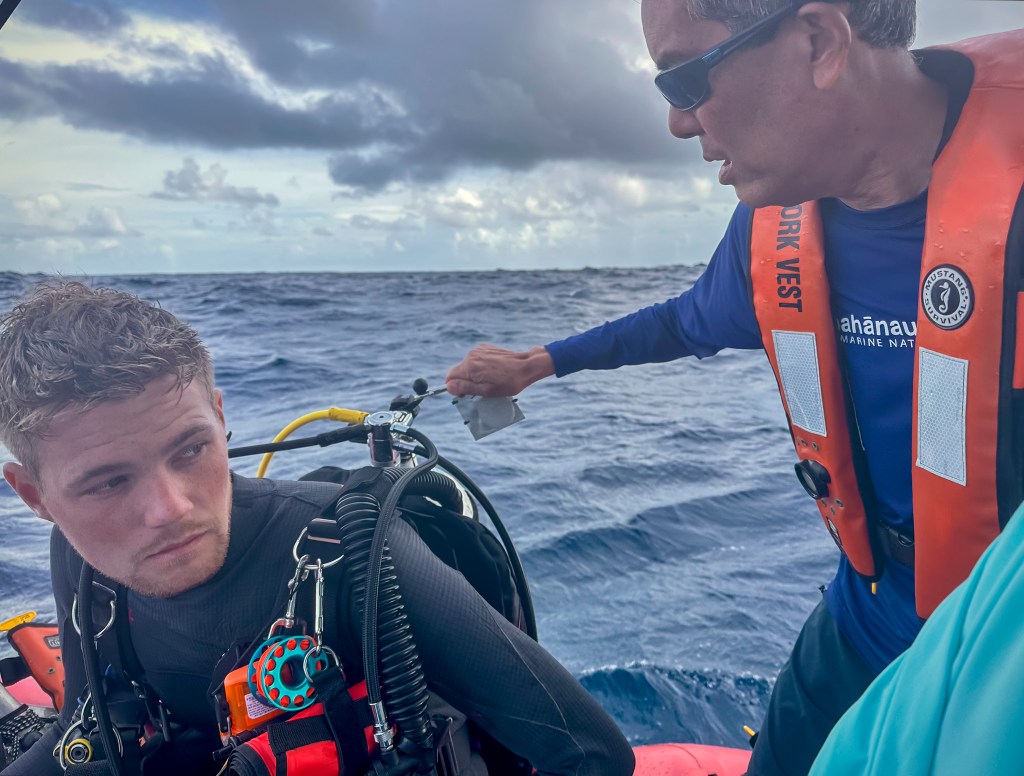 Randy Kosaki clips an eDNA test to the scuba tank on the back of scientist Makoa Pascoe to detect chondria in the Northwestern Hawaiian Islands. (Nathan Eagle/Civil Beat/2024)
