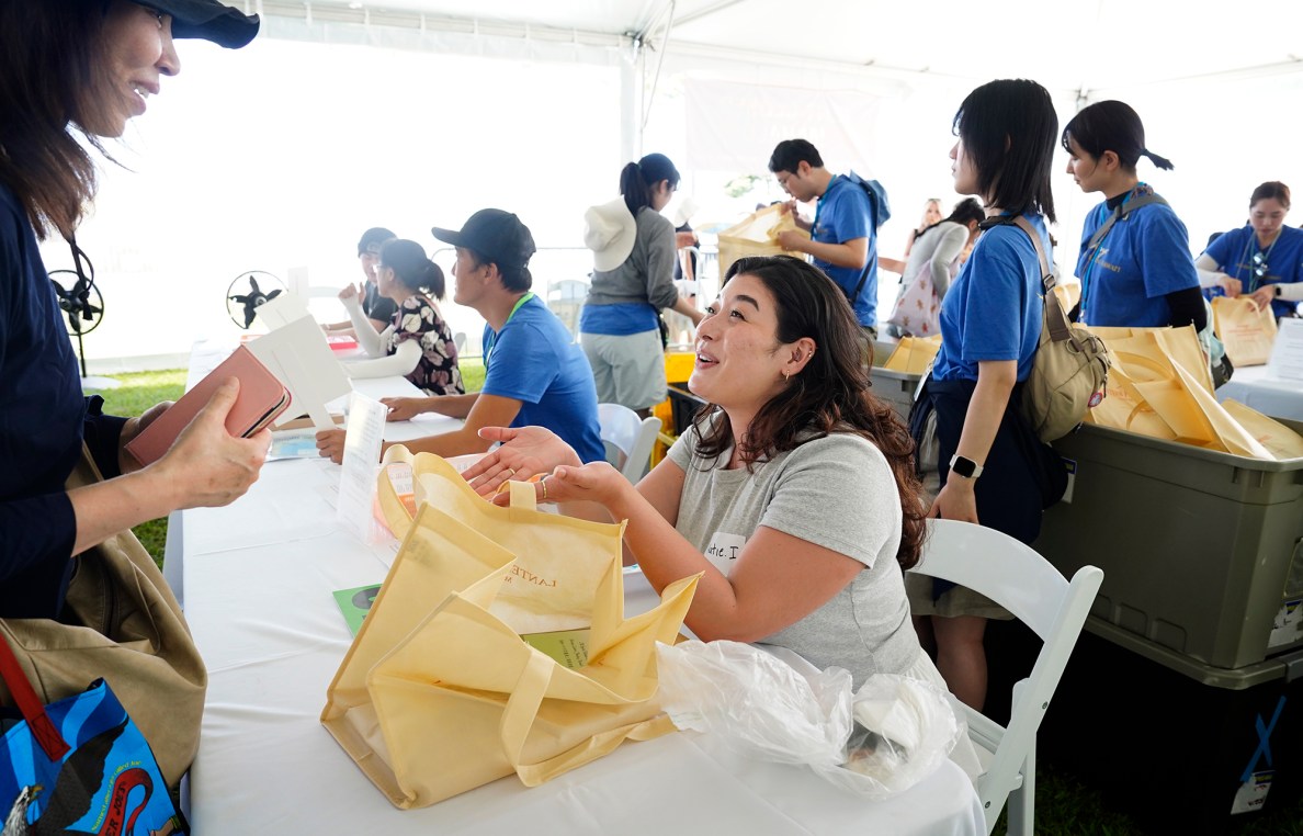 Shinnyo-en USA practitioner Katie Ishizaka, of Chicago, goes over instructions with Yamazaki Hiroko, of Tokyo, as she picks up her floating lantern for the 27th Annual Shinnyo Lantern Floating Hawaiʻi Monday, May 26, 2025, at Ala Moana Regional Park in Honolulu. 6,000 lanterns with messages to lost loved ones are launched by family members. This is the third year Ishizaka has volunteered to help with the annual event. (Kevin Fujii/Civil Beat/2025)