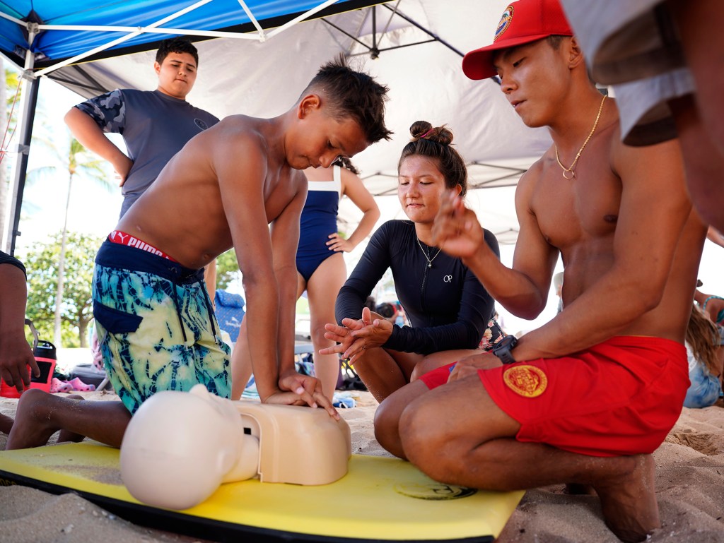 Micah McNiel, 12, does chest compressions during the Honolulu Ocean Safety Department’s Junior Lifeguard Program’s CPR section as lifeguard Jedidiah Wataru counts for timing at Ko’olina Wednesday, June 25, 2025, in Kapolei. (Kevin Fujii/Civil Beat/2025)