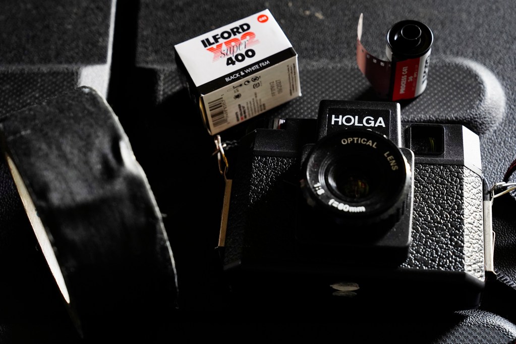 Moving clockwise: a Holga 120 toy film camera, a roll of gaffer’s tape a box and roll of Ilford XP2 black-and-white 35mm film are photographed Tuesday, June 15, 2025, in ʻEwa Beach. Photographs for John Hill’s project on child abuse were made with these items. (Kevin Fujii/Civil Beat/2025)