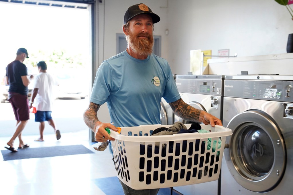 Maui Rescue Mission executive director Scott Hansen takes freshly washed laundry to a dryer Wednesday, July 23, 2025, in Kahului. He’s washing clothes for residents of Pu‘uhonua a Nene, a Kahului kauhale. Hansen knew Rex Cole, a homeless man who died in the Aug. 8, 2023, fire in Lahaina. (Kevin Fujii/Civil Beat/2025)