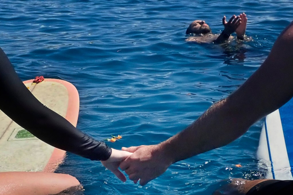 Jess Faust, left, holds hands with Taylor Giordani during the  memorial paddle-out from Hanaka‘ō‘ō Beach Park Friday, Aug. 8, 2025, in Lahaina. Faust lived in Lahaina before the fire. 102 people died in the Aug. 8, 2023, fire which destroyed the historic West Maui town and Upcountry. (Kevin Fujii/Civil Beat/2025)
