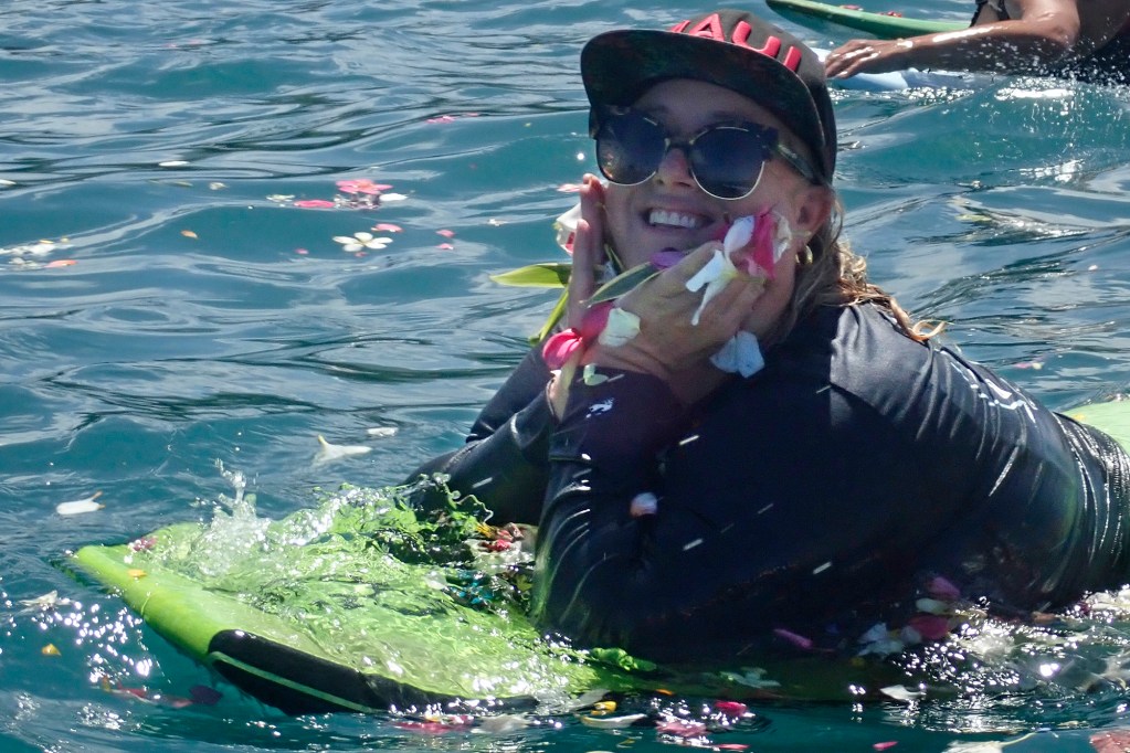 Memorial paddle-out participant Cassie Coonradt stops for a photo with the flowers off Hanaka‘ō‘ō Beach Park Friday, Aug. 8, 2025, in Lahaina. 102 people died in the Aug. 8, 2023, fire which destroyed the historic West Maui town and Upcountry. (Kevin Fujii/Civil Beat/2025)