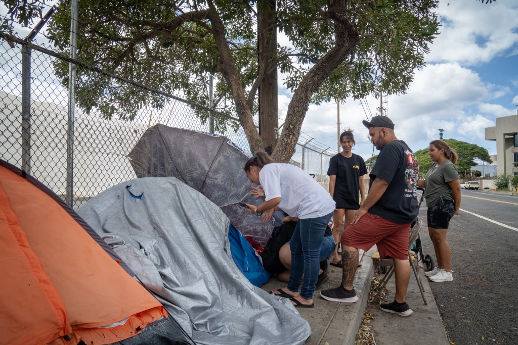 Relatives of Kuuipo Surls-Kane coax their loved one from a tent at the Sand Island section of Honolulu, Saturday, Aug. 16, 2025. Surls-Kane, who is unhoused in Hilo, was flown to The Queen’s Medical Center in Honolulu for injuries. She subsequently departed the hospital and her relatives had been searching for her after finding out she had been flown to Honolulu. She was found today. (Craig Fujii/Civil Beat/2025)