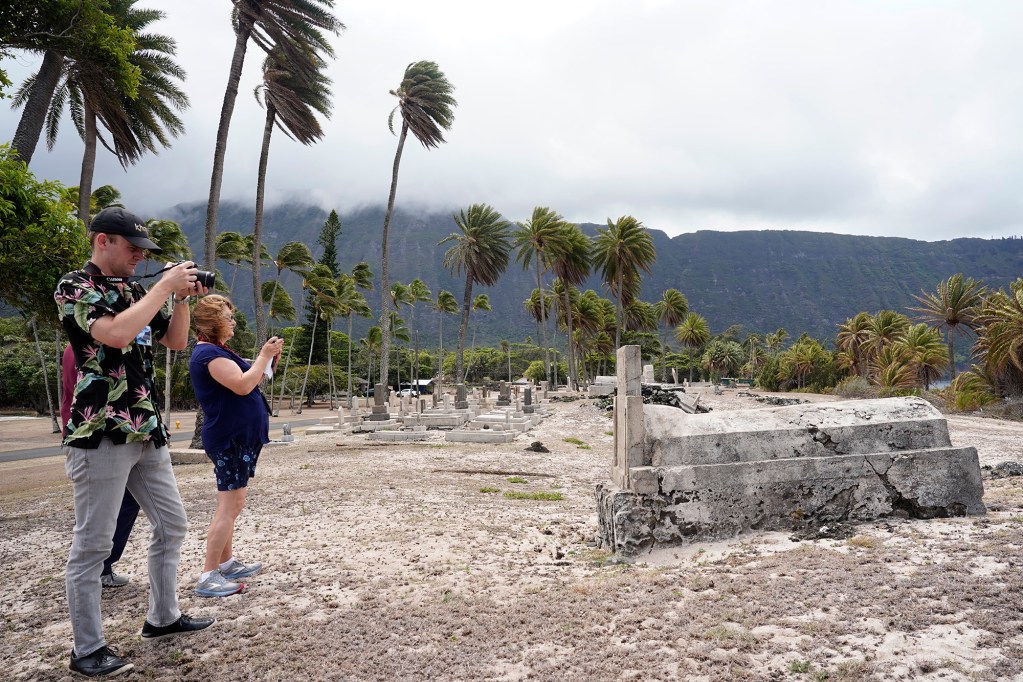 Bryce Moore, from left, and Allison Schaefers photograph one of the many Papaloa Cemetery graves during the Kalaupapa Saints Tour Thursday, Sept. 18, 2025, in Kalaupapa. Covid closed Kalaupapa National Historical Park five years ago. Multiple state and federal agencies coordinated to allow a patient-owned tour company to bring visitors back. (Kevin Fujii/Civil Beat/2025)