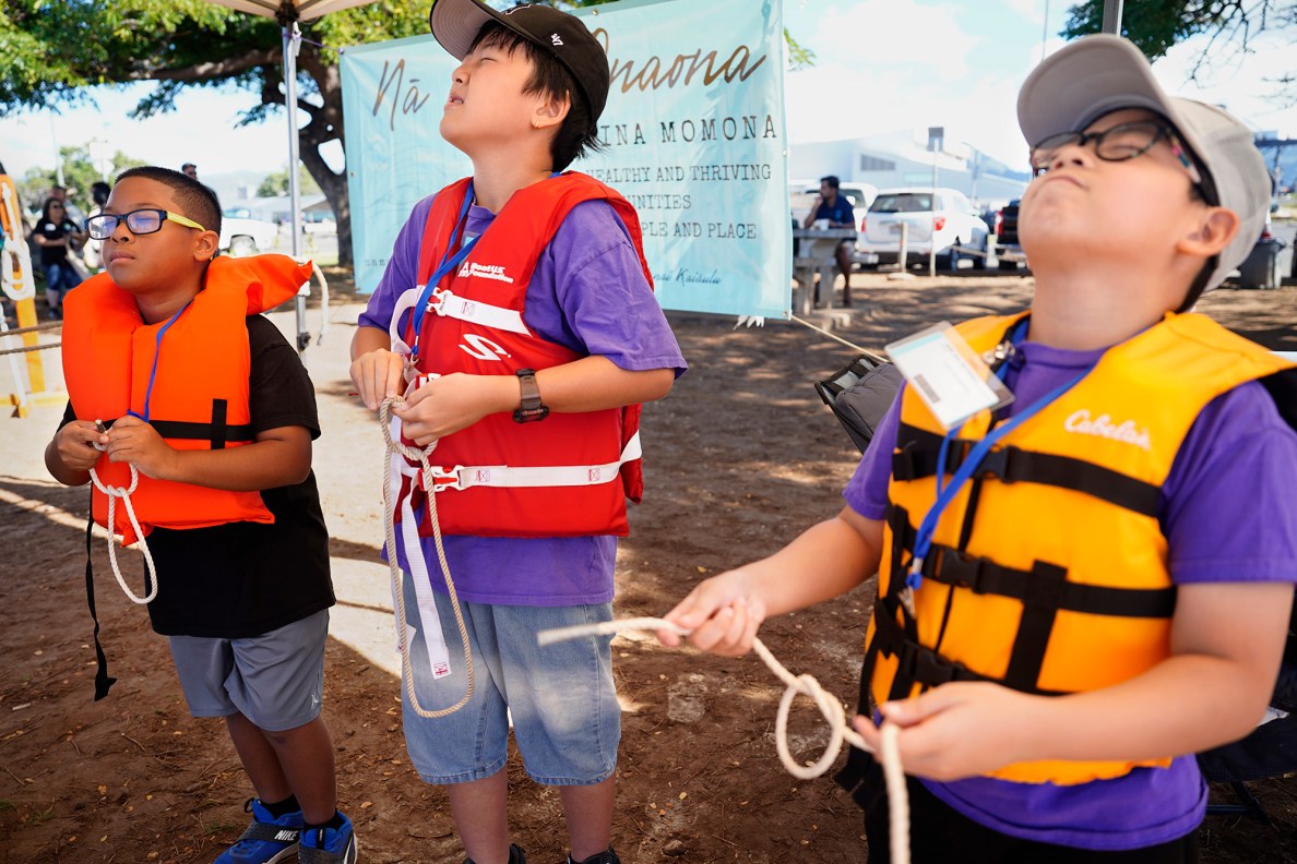 Kapālama Elementary School 4th graders Rixon Allgood-Pascual, from left, Johnny Chen and Kian Reyes close their eyes to mimic nighttime while trying square knots during the  Ho‘ākea Honolulu hands-on learning and experiencing event centered around traditional Hawaiʻian navigation and voyaging canoes Wednesday, Dec. 3, 2025, in Honolulu. Hawaiʻian voyaging traditions, cultural practices and ʻāina-based learning pairs with DOE curriculum to create a “Navigator Mindset”. (Kevin Fujii/Civil Beat/2025)