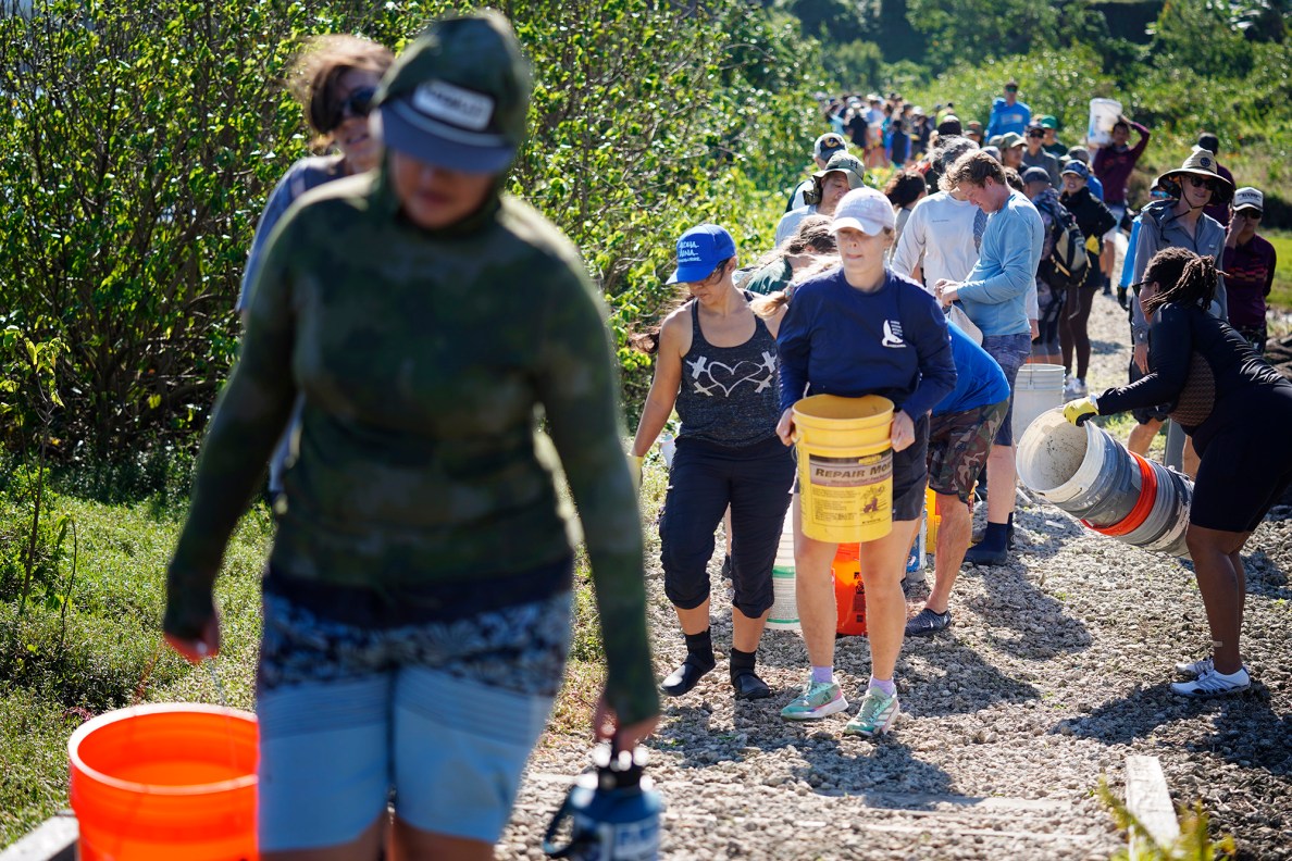 Some of the 2,000 volunteers walk buckets of ko‘a (coral) pieces for Moʻokuapā, a Paepae O He‘eia event to complete re-building the wall surrounding the He‘eia loko i‘a (fishpond) Saturday, Dec. 13, 2025, in Kāneʻohe. The volunteers joined the Moʻokuapā community work day event to support the 800-year-old He‘eia loko i‘a. (Kevin Fujii/Civil Beat/2025)