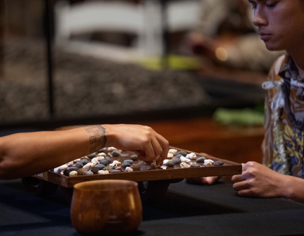 An all-Oʻahu championship match between Kapena Baptista, right, makes a move under the watchful eyes of Kahekili Yung, during the inaugural Ka Makou Kōnane Invitational Tournament in the center of the Bishop Museum’s Hawaiʻian Hall Friday, Feb. 13, 2026, in Honolulu. (Kevin Fujii/Civil Beat/2026)