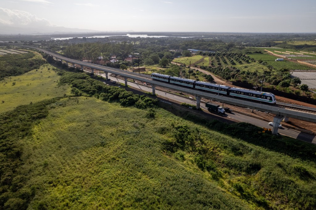 An elevated rail train are seen surrounded by farm and other less developed land.