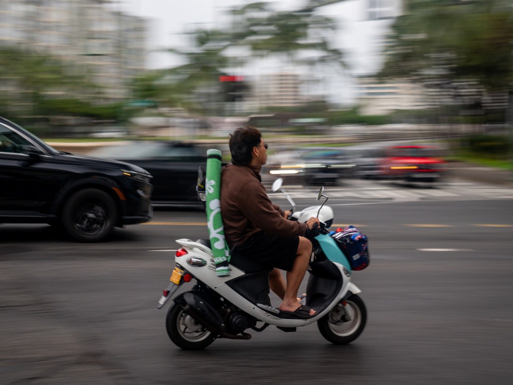 An unhelmeted moped rider on Kalakaua Avenue in Waikiki April 13, 2026. (Craig Fujii/Civil Beat/2026)